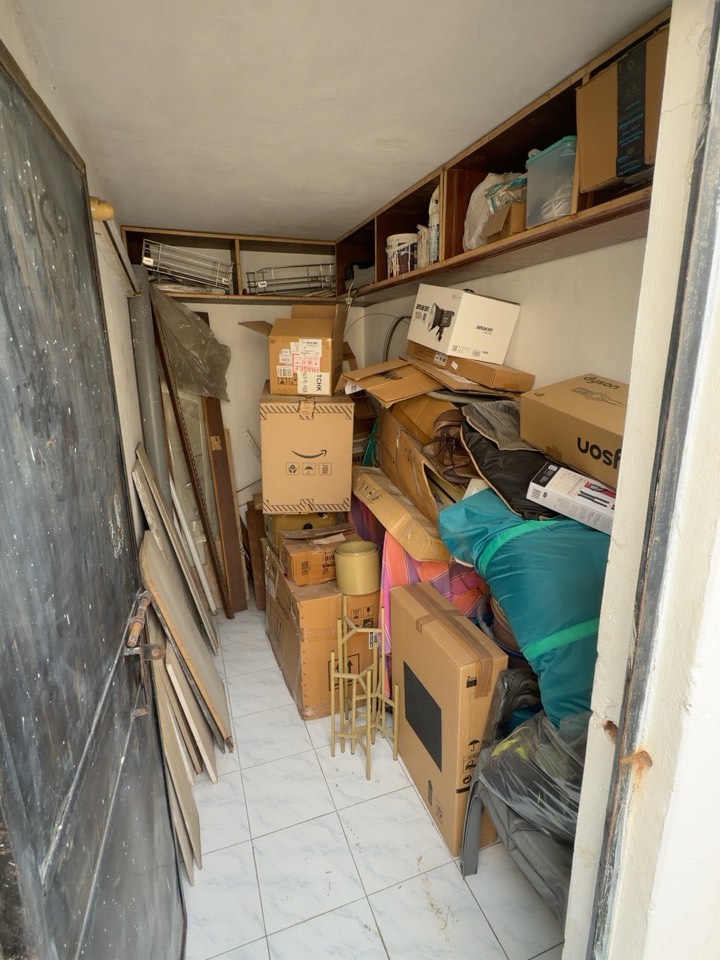 The room before work begins, viewed from the doorway, with boxes and bags beneath the overhead shelves.